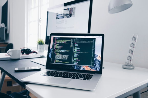 a-mac-book-with-lines-of-code-on-its-screen-on-a-busy-desk.jpg A MacBook with lines of code on its screen on a busy desk
